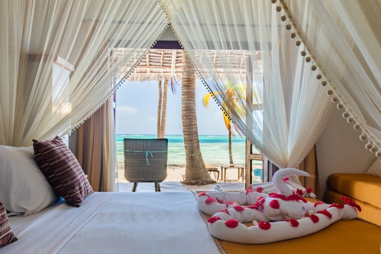 Bed facing the sea through open doors in a beachfront room at Karafuu