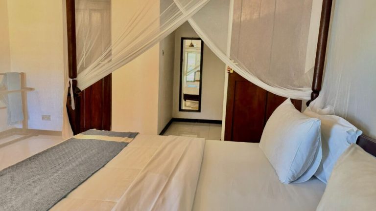 Double bed under a mosquito net in a cottage room at Flame Tree Cottages