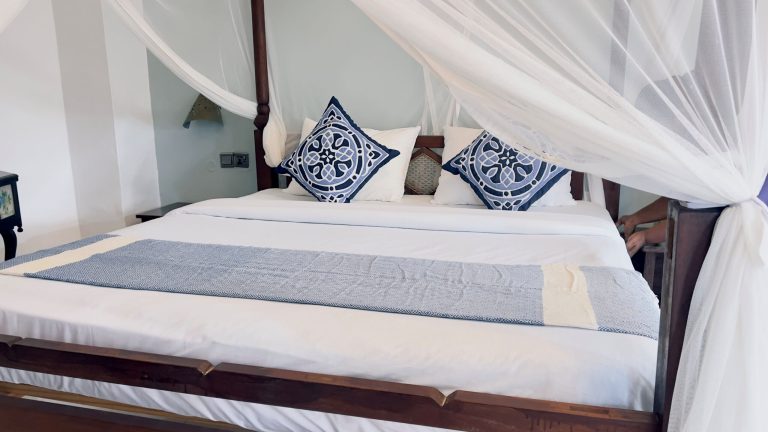 Zanzibari four-poster bed with mosquito net at Flame Tree Cottages