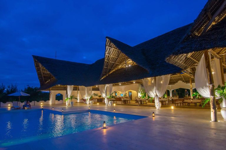 Thatched restaurant and pool lit at night at Konokono Beach Resort